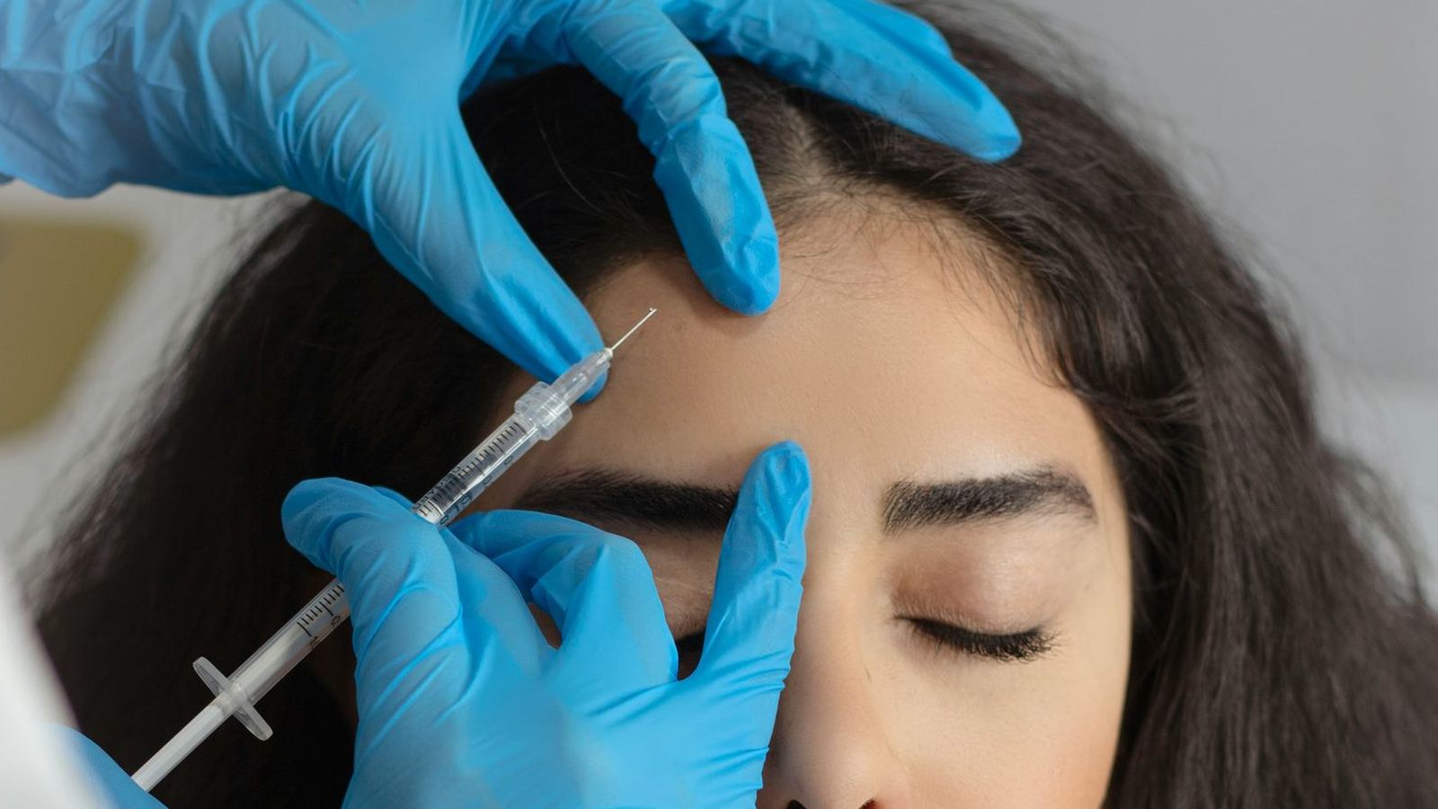 A gloved provider administering an injection near a patient's brow during a medical aesthetics treatment