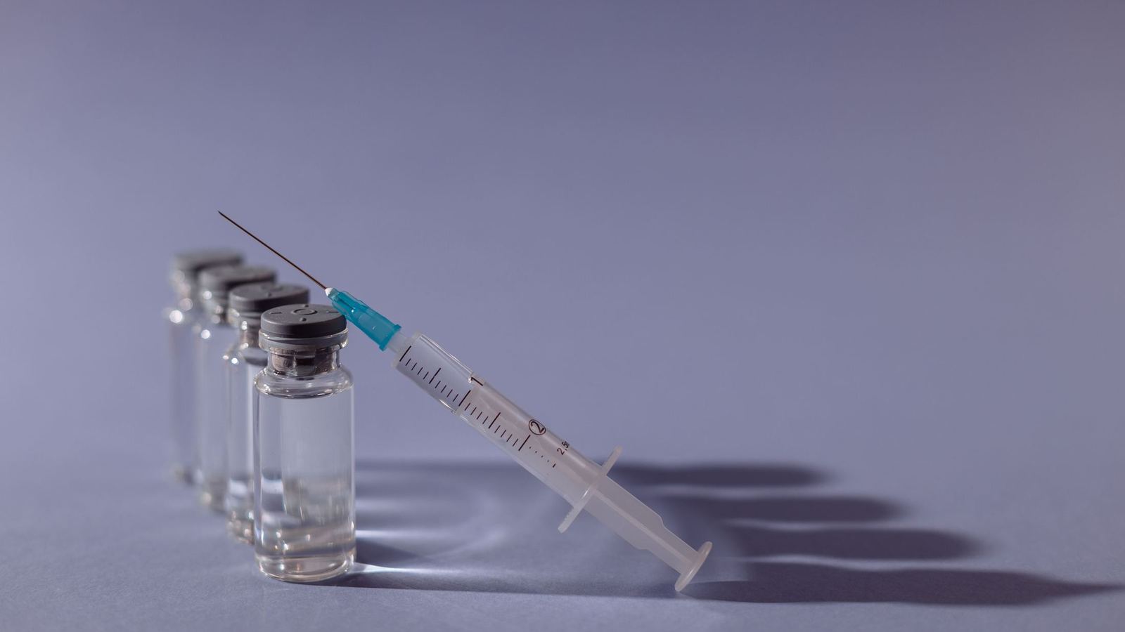 Small glass medication vials beside a syringe on a lavender background